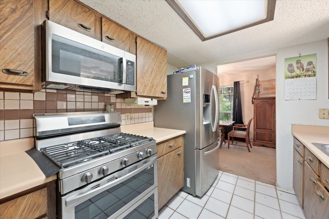 Kitchen featuring backsplash, light tile patterned floors, stainless steel appliances, and a textured ceiling | Image 18