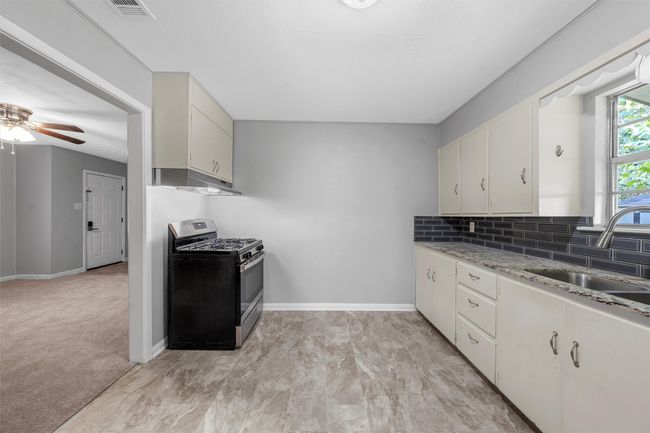 Kitchen with gas stove, under cabinet range hood, backsplash, ceiling fan, and light stone countertops | Image 7