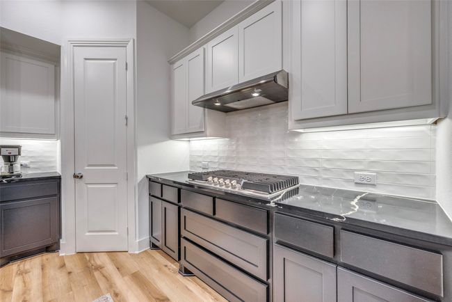 Kitchen featuring light wood-style floors, under cabinet range hood, tasteful backsplash, and stainless steel gas stovetop | Image 11