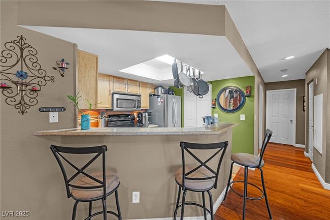 Kitchen with light countertops, wood finished floors, a kitchen breakfast bar, appliances with stainless steel finishes, and baseboards | Image 8