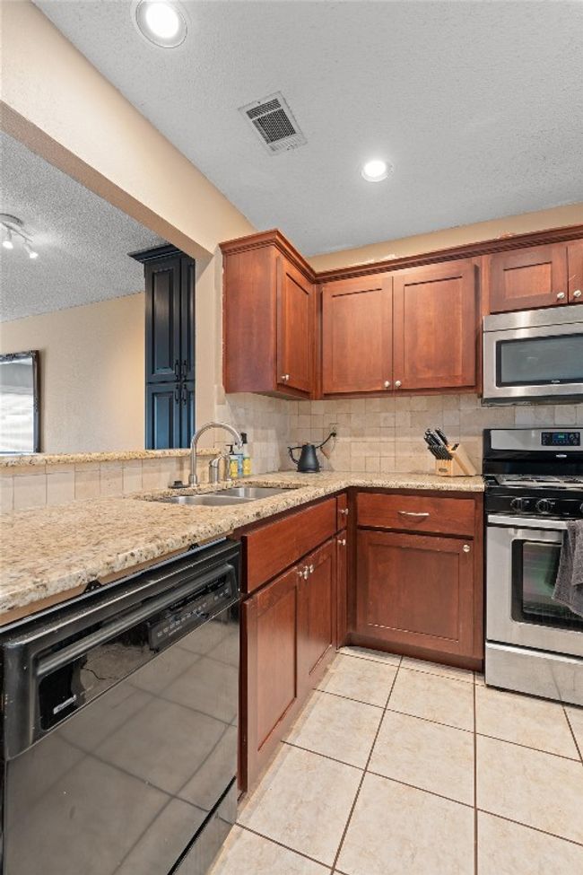 Kitchen with appliances with stainless steel finishes, a textured ceiling, decorative backsplash, light stone countertops, and light tile patterned flooring | Image 10