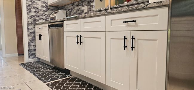 Kitchen with white cabinets, tile patterned flooring, dark stone countertops, and decorative backsplash | Image 10