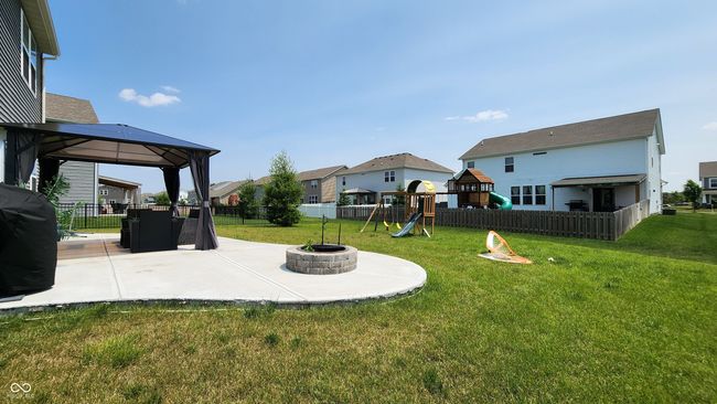 fenced backyard featuring a gazebo, a playground, a fire pit, a residential view, and a patio area | Image 23