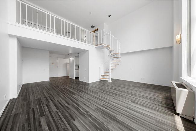 Unfurnished living room featuring stairs, wood finished floors, a towering ceiling, baseboards, and radiator | Image 12