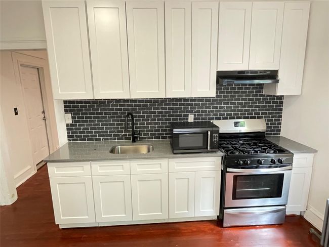 Kitchen with stainless steel range with gas cooktop, a sink, under cabinet range hood, dark wood-style floors, and decorative backsplash | Image 11