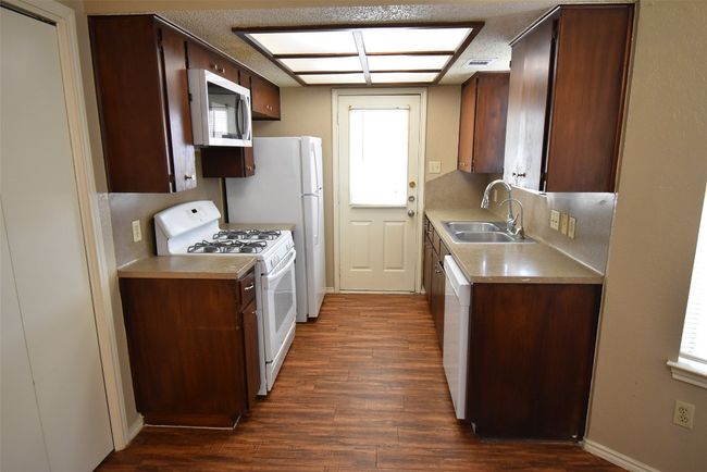 Kitchen with white appliances, dark wood-style floors, light countertops, and dark brown cabinetry | Image 5