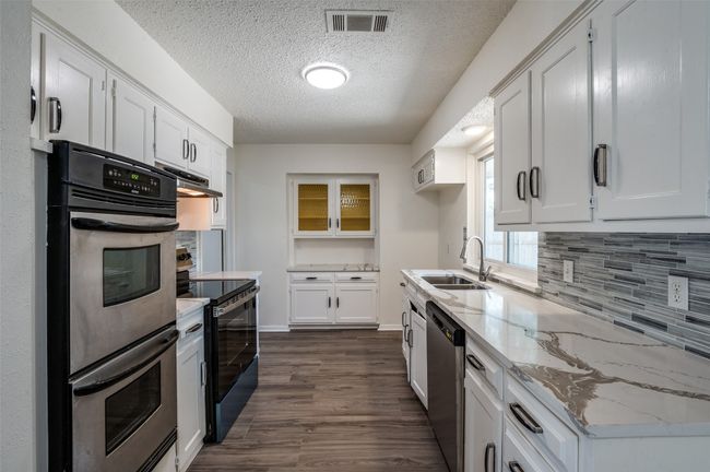 Kitchen featuring stainless steel appliances, under cabinet range hood, tasteful backsplash, white cabinets, and dark wood-type flooring | Image 8