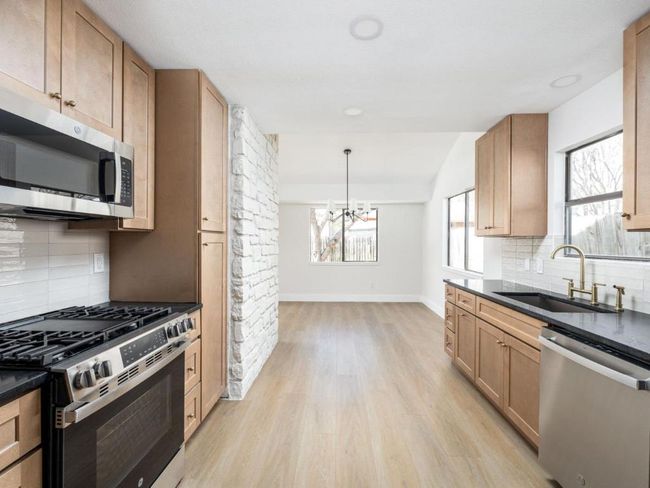 Kitchen with light wood finished floors, an inviting chandelier, a sink, appliances with stainless steel finishes, and dark countertops | Image 17