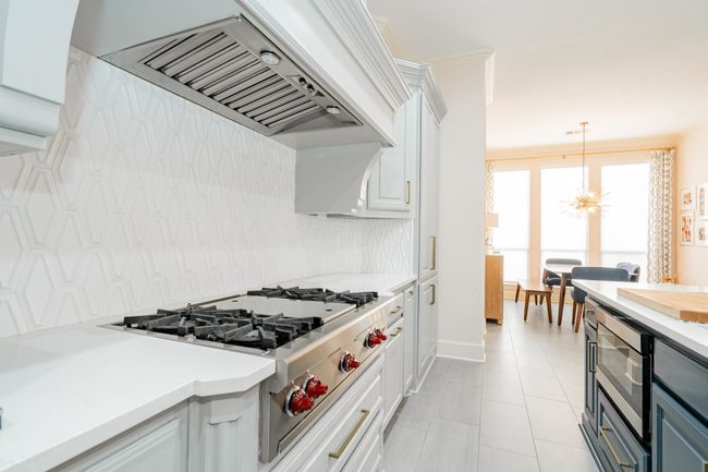 Kitchen with tasteful backsplash, white cabinetry, custom range hood, light countertops, and appliances with stainless steel finishes | Image 8