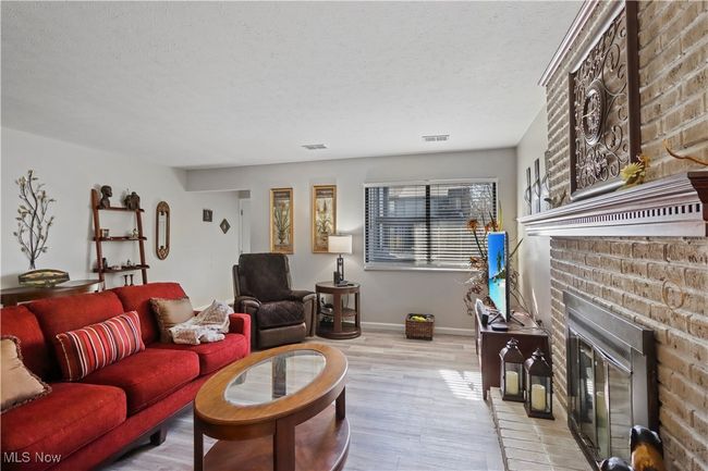 Living area featuring light wood-style flooring, a fireplace, baseboards, visible vents, and a textured ceiling | Image 11