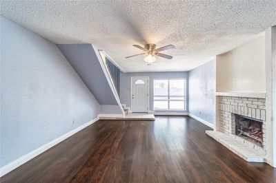 Unfurnished living room with a fireplace, dark wood-type flooring, a textured ceiling, and ceiling fan | Image 3