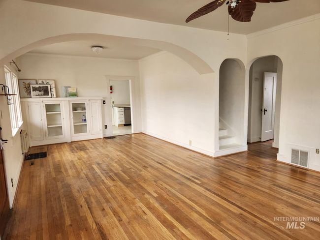 Unfurnished room with arched walkwayDs, light wood-style flooring, crown molding, a ceiling fan, and stairway | Image 5