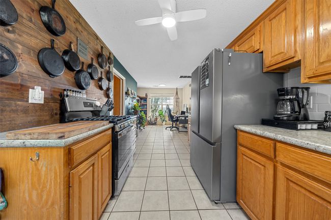 Kitchen with brown cabinetry, ceiling fan, stainless steel appliances, and light tile patterned floors | Image 13