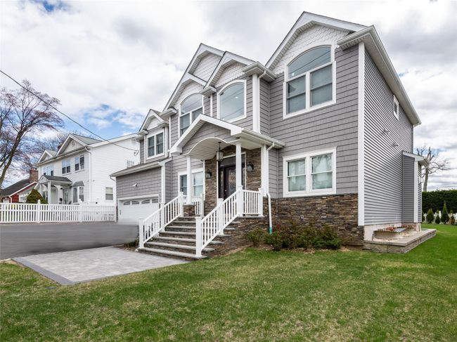 View of front facade with fence, a front lawn, an attached garage, driveway, and stone siding | Image 25