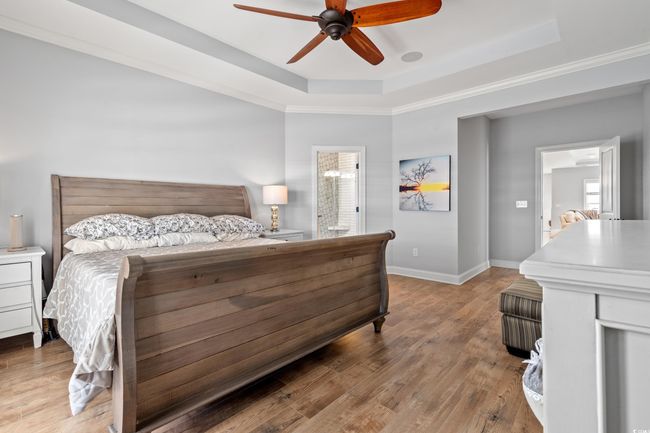 Bedroom with a tray ceiling, light wood-type flooring, a ceiling fan, ensuite bath, and crown molding | Image 13