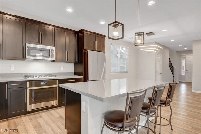Kitchen with stainless steel appliances, light wood finished floors, light countertops, dark brown cabinets, and recessed lighting | Image 18