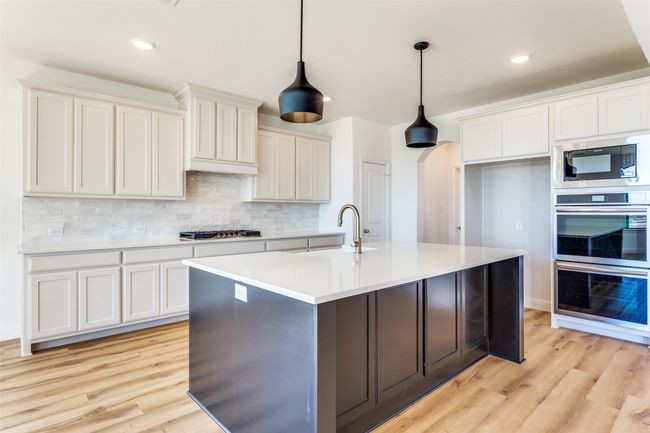 Kitchen featuring appliances with stainless steel finishes, an island with sink, light hardwood / wood-style flooring, and tasteful backsplash | Image 7