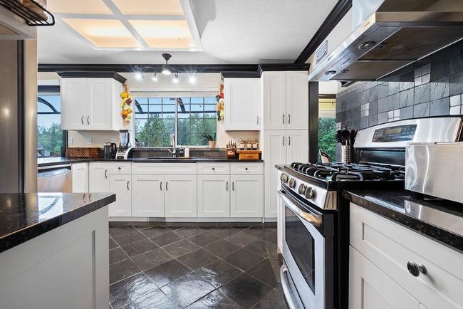 Kitchen with stainless steel appliances, wall chimney range hood, white cabinetry, and a sink | Image 13