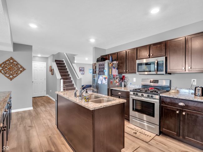 kitchen featuring appliances with stainless steel finishes, dark brown cabinetry, light wood finished floors, and a sink | Image 7