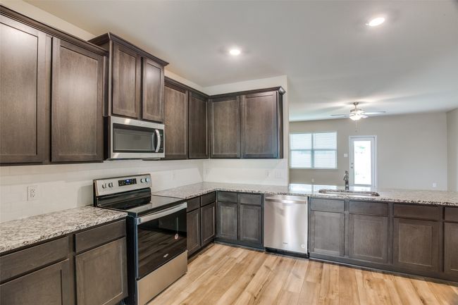 Kitchen featuring dark brown cabinets, stainless steel appliances, a ceiling fan, and a sink | Image 4