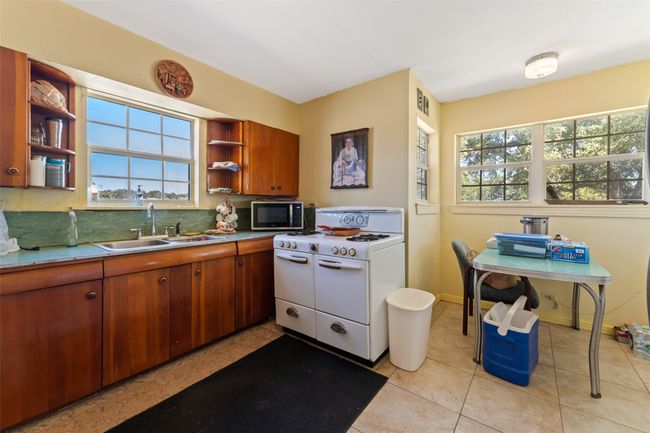 Kitchen featuring brown cabinets, open shelves, stainless steel microwave, a sink, and white gas range oven | Image 9