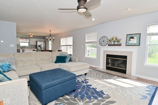 living area featuring a chandelier, ceiling fan, a tile fireplace, a textured ceiling, and baseboards | Image 11