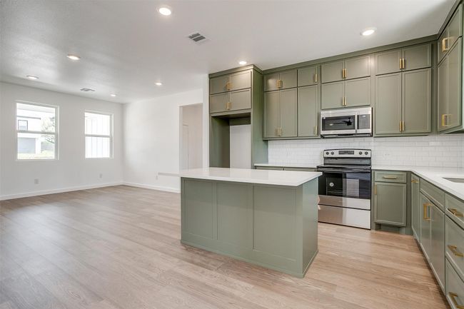 Kitchen with green cabinets, a kitchen island, visible vents, decorative backsplash, and stainless steel appliances | Image 11