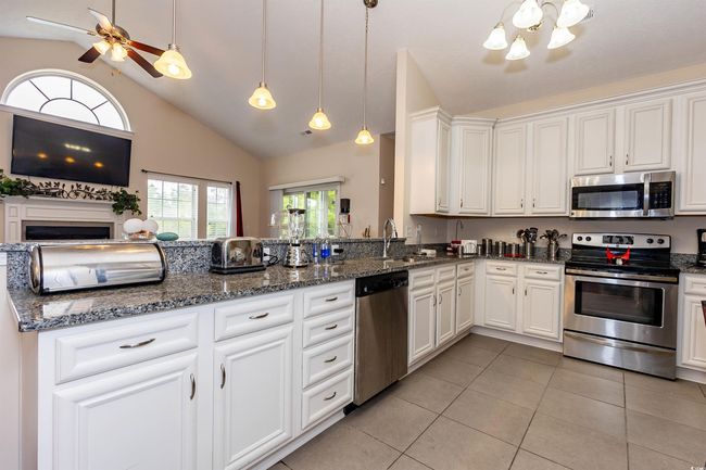 Kitchen with a sink, light tile patterned floors, stainless steel appliances, white cabinets, and lofted ceiling | Image 9