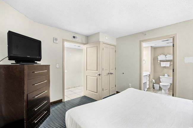 Bedroom with light tile patterned flooring, connected bathroom, a closet, and visible vents | Image 12