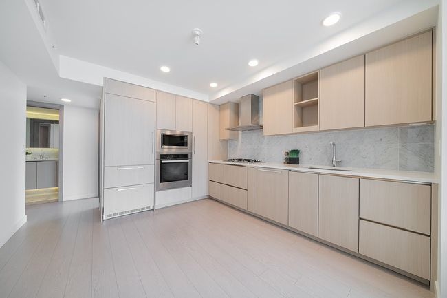 Kitchen with stainless steel appliances, wall chimney exhaust hood, light countertops, open shelves, and light brown cabinets | Image 4