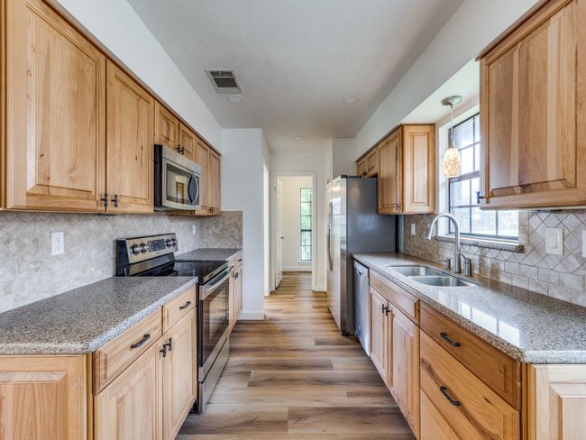 Kitchen with appliances with stainless steel finishes, light wood-type flooring, light stone counters, and tasteful backsplash | Image 10