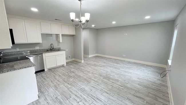 Kitchen with stainless steel dishwasher, white cabinets, light wood-style floors, a chandelier, and recessed lighting | Image 5