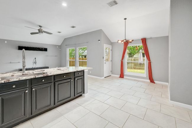 Kitchen featuring visible vents, baseboards, a ceiling fan, light stone countertops, and lofted ceiling | Image 14