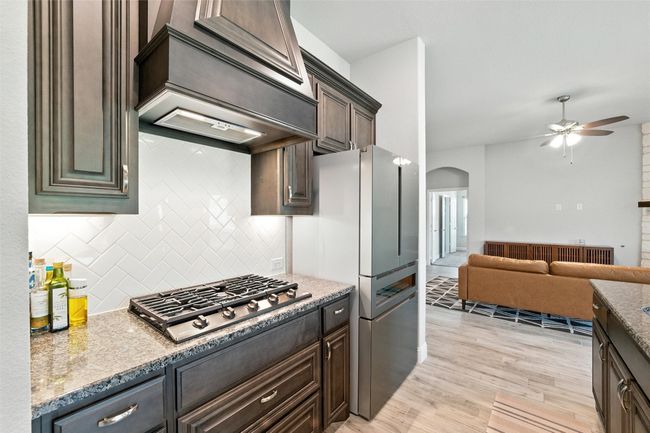 Kitchen featuring arched walkways, a ceiling fan, decorative backsplash, custom range hood, and open floor plan | Image 15