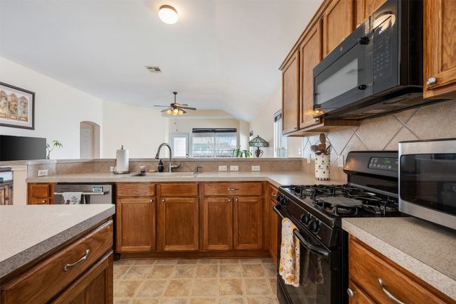 Kitchen featuring visible vents, black appliances, a ceiling fan, a sink, and brown cabinetry | Image 19