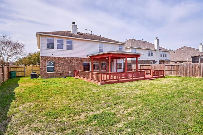 This photo showcases a spacious backyard with a large wooden deck attached to a two-story house. The home features a combination of brick and siding, and the yard is fenced, providing privacy. It's ideal for outdoor entertaining and relaxation. | Image 43