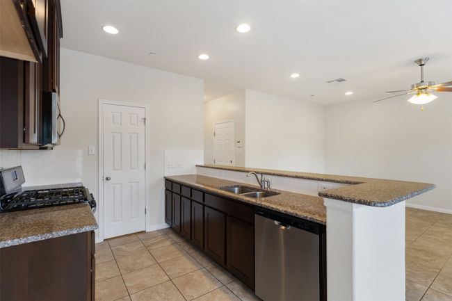 Kitchen with stainless steel appliances, a peninsula, light tile patterned floors, decorative backsplash, and dark brown cabinets | Image 11
