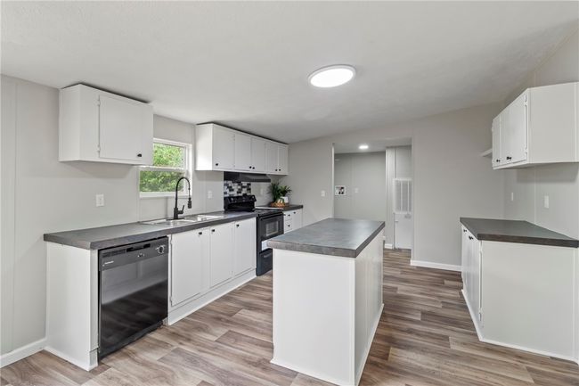 Kitchen featuring dark countertops, light wood finished floors, a sink, and black appliances | Image 8