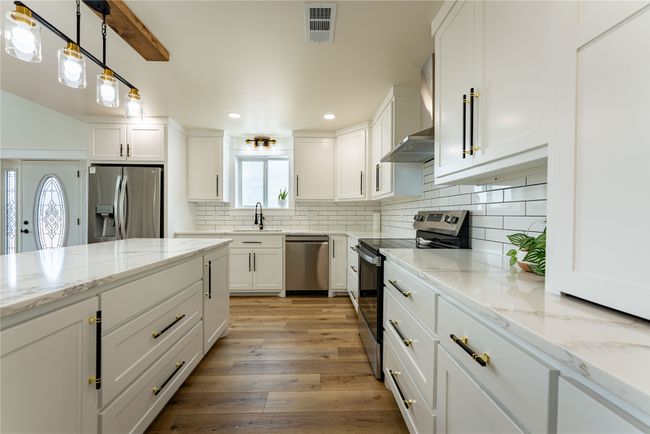 Kitchen with visible vents, light wood-style flooring, appliances with stainless steel finishes, wall chimney range hood, and backsplash | Image 5