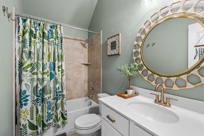 Full bathroom featuring a textured wall, shower / bath combination with curtain, toilet, vanity, and lofted ceiling | Image 18