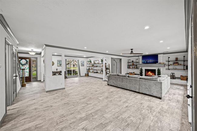 This spacious living area features modern tile flooring, a cozy fireplace, and a large sectional sofa. The room is well-lit with recessed lighting and natural light from large windows. Stylish built-in shelves provide ample storage and display space. | Image 13