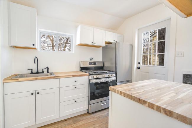 Kitchen with light wood-style flooring, a sink, butcher block countertops, stainless steel appliances, and white cabinets | Image 7