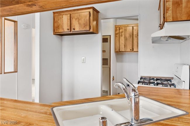 Kitchen featuring brown cabinets, a sink, light countertops, under cabinet range hood, and gas range gas stove | Image 15