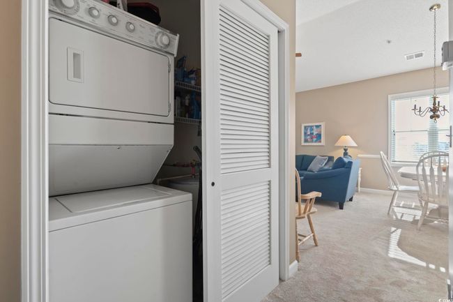 Laundry room featuring stacked washer / drying machine, light carpet, baseboards, and a chandelier | Image 24