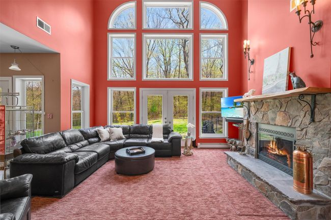 Living area featuring visible vents, a towering ceiling, a stone fireplace, plenty of natural light, and french doors | Image 10
