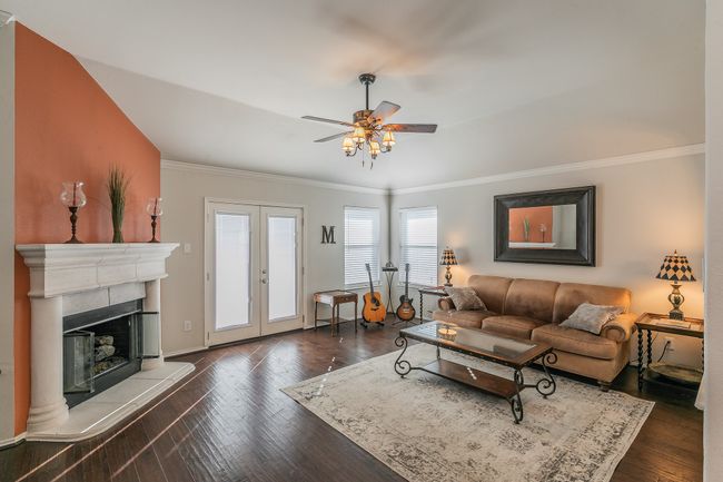 Living area with french doors, a fireplace with raised hearth, dark wood-style floors, and crown molding | Image 10