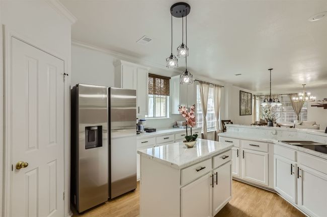 Kitchen with stainless steel refrigerator with ice dispenser, light wood-style flooring, white cabinetry, decorative light fixtures, and a center island | Image 7