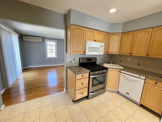 Kitchen featuring light tile patterned floors, white appliances, a sink, a baseboard radiator, and light brown cabinets | Image 7