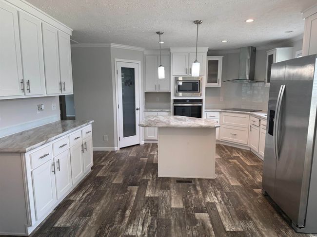 Kitchen with stainless steel appliances, wall chimney range hood, a textured ceiling, white cabinets, and ornamental molding | Image 14