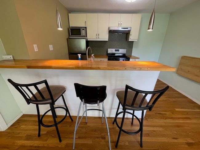 Kitchen with under cabinet range hood, appliances with stainless steel finishes, butcher block countertops, backsplash, and wood finished floors | Image 7